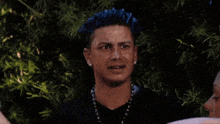 a man with blue hair is making a funny face while another man holds his hand out towards him .