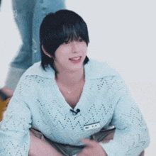a young man with long black hair is wearing a blue sweater and smiling .