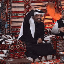 two men are sitting on a couch and one is wearing a white scarf around his head