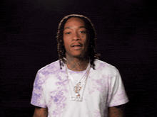 a man wearing a purple tie dye shirt has a necklace that says cam on it