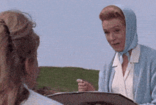 a woman in a blue scarf is talking to another woman in a field