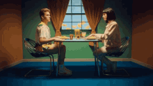 a man and a woman are sitting at a table in front of a window with the letters c and e visible
