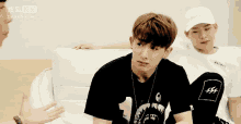 two young men are sitting on a white couch talking to each other . one of the men is wearing a number 1 shirt .