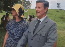 a man in a suit and tie stands next to a woman wearing a yellow hat