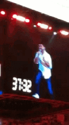 a man singing into a microphone in front of a large screen that says ' eele ' on it