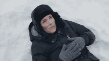a woman wearing a hat and gloves laying in the snow