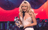 a woman in a white dress holds a microphone and a trophy