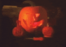a carved pumpkin is lit up in the dark with two smaller pumpkins behind it