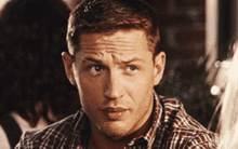 a man in a plaid shirt looks at the camera with a serious look on his face