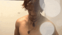 a shirtless man with a necklace around his neck is standing in front of a white wall