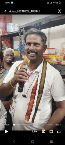 a man in a white shirt is holding a microphone in front of a cell phone screen that says video_20240929_1838465