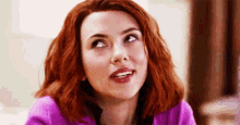 a close up of a woman with red hair wearing a purple shirt and smiling .