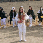 a woman in white pants and a red vest stands in front of a group of people