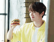 a man in a yellow shirt is holding a hamburger in his hand