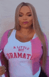 a woman wearing a pink cardigan and a white tank top with the words `` a little bit drama '' on it .