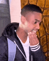 a young man is covering his mouth with his hand while wearing a black jacket .