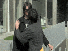 a man wearing sunglasses and a black jacket is hugging another man