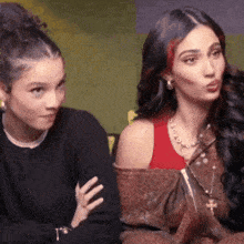 two women are sitting next to each other and one of them is wearing a red tank top