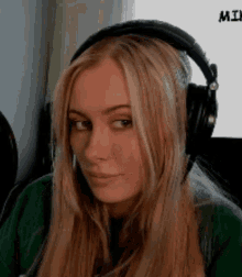 a woman wearing headphones and a green sweater is making a funny face .