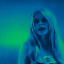 a woman with long blonde hair is standing in a dark room with a blue and green background