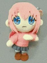 a stuffed doll with pink hair and blue eyes is sitting on a table .