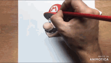 a hand is drawing mario with a red pencil