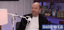 a man is sitting in front of a microphone with a sign that says dark web on it .