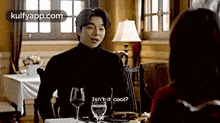 a man in a black turtleneck is sitting at a table with a woman and talking to her .