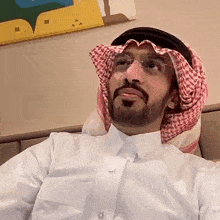 a man with a beard wearing a white shirt and a head scarf is sitting on a bed .