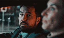 a man with a beard is driving a car with a woman looking out the window .