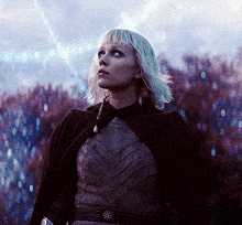 a woman with blonde hair is wearing a black cape and looking up