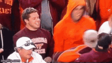 a man wearing a virginia tech shirt stands in a crowd of people .