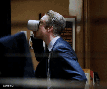 a man in a suit and tie drinking from a cup with the word carisibot written below him