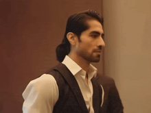 a man with long hair and a ponytail is wearing a white shirt and a black vest