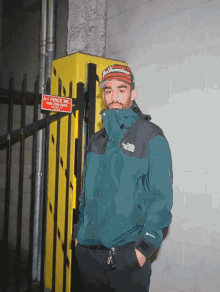 a man in a north face jacket stands in front of a yellow fence