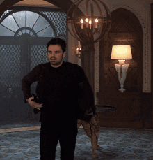 a man in a black shirt is standing in a room with a lamp