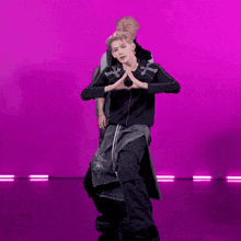 a man in a black jacket with a cross on it is dancing in front of a pink background