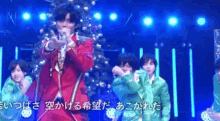 a man in a red suit is singing into a microphone on a stage with a christmas tree in the background