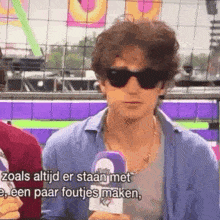 a man wearing sunglasses is holding a microphone and talking to someone .