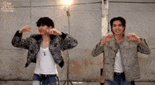 two men are standing next to each other making a heart shape with their hands