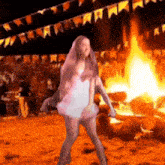 a woman in a white dress is dancing in front of a burning fire