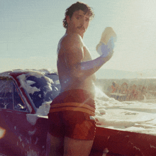 a shirtless man in red shorts is washing a car