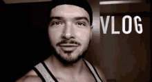 a man with a beard is wearing a beanie and a tank top with the word vlog written on the bottom