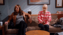 two women are sitting on a couch in a room with a tissue box