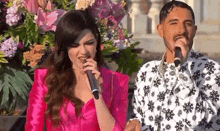 a woman in a pink jacket is singing into a microphone next to a man in a white shirt with snowflakes on it .