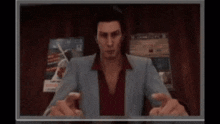 a man in a suit and red shirt is sitting in front of a television .