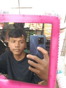 a man is taking a selfie in front of a pink mirror with a display of snacks behind him
