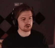 a man with a beard wearing headphones is sitting in front of a computer screen .