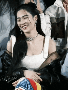a woman wearing a white tank top and a black jacket smiles