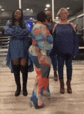 a woman in a blue dress is hugging another woman in an orange and blue outfit